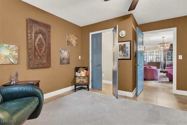 sitting room with tile patterned floors, baseboards, and ceiling fan with notable chandelier