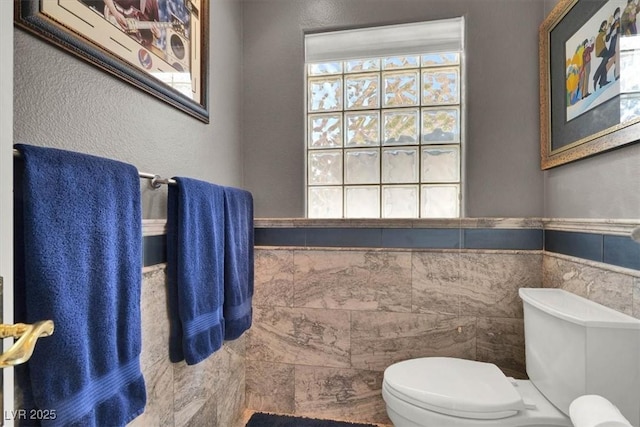 bathroom featuring tile walls, toilet, and wainscoting