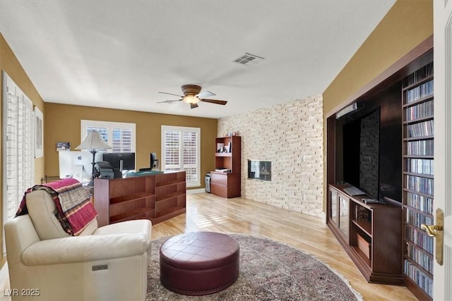 living room with visible vents, a ceiling fan, built in features, light wood-style floors, and a brick fireplace