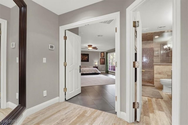 hall featuring visible vents, baseboards, and wood finished floors