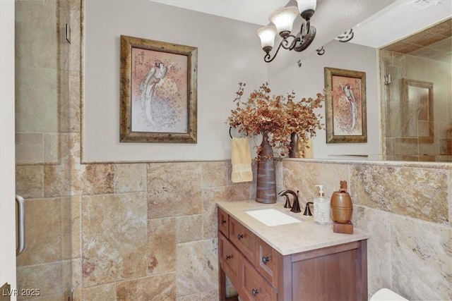 bathroom with a notable chandelier, a tile shower, tile walls, wainscoting, and vanity