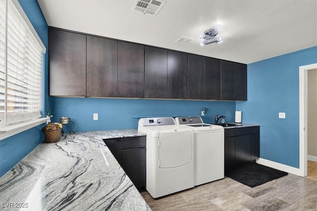 clothes washing area with visible vents, washing machine and clothes dryer, light wood-style flooring, cabinet space, and a sink