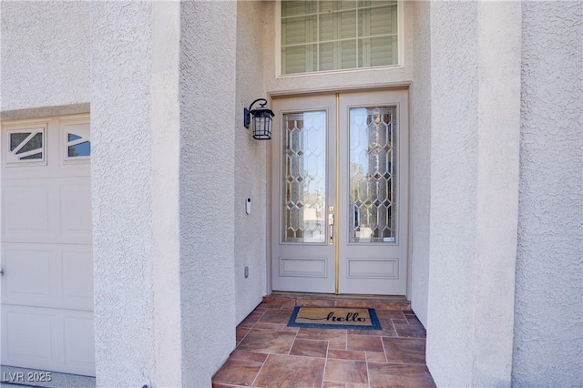 view of exterior entry with a garage and stucco siding