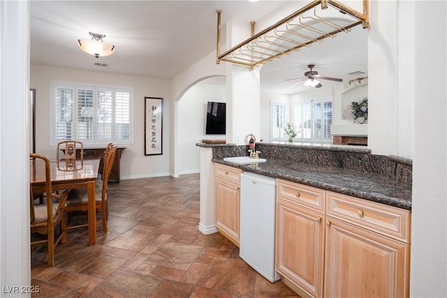 kitchen featuring light brown cabinets, baseboards, arched walkways, white dishwasher, and a sink