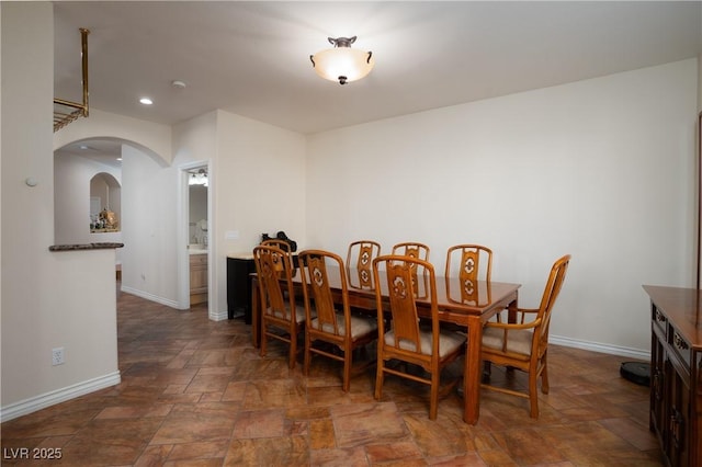 dining room featuring arched walkways, recessed lighting, stone finish floor, and baseboards