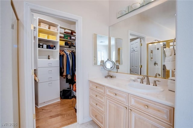 bathroom with a stall shower, vanity, a walk in closet, and wood finished floors