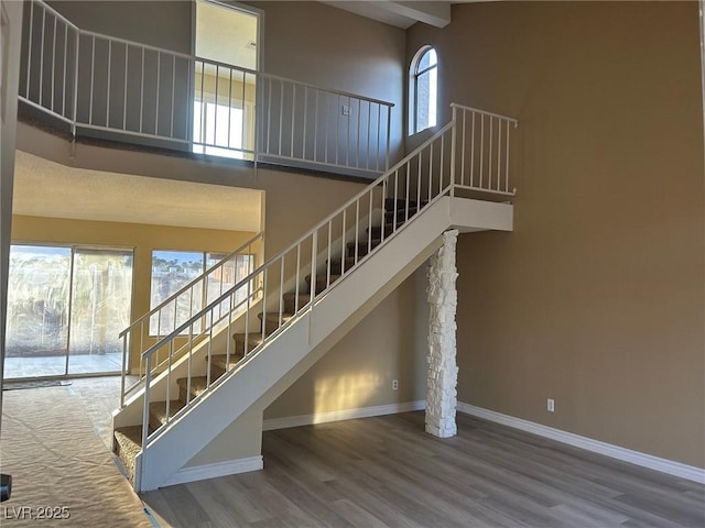 staircase featuring baseboards, a high ceiling, and wood finished floors