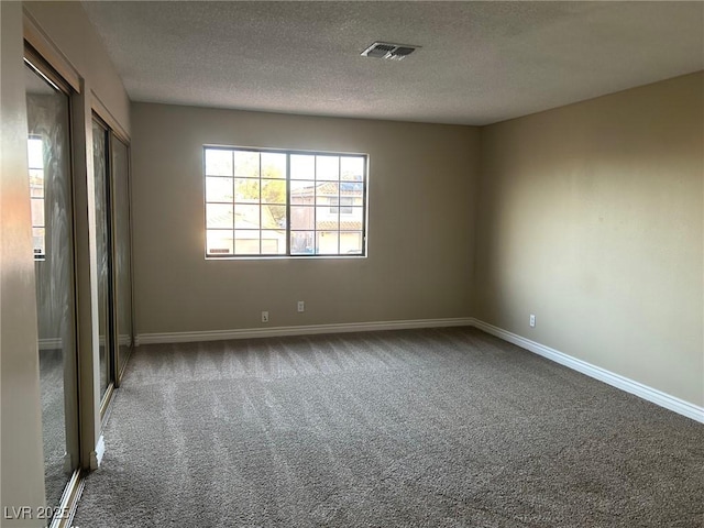 carpeted spare room with visible vents, a textured ceiling, and baseboards