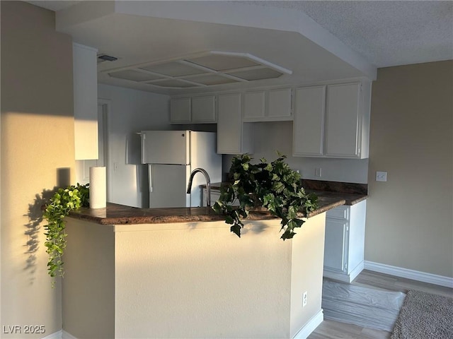 kitchen featuring visible vents, baseboards, light wood-style flooring, a peninsula, and freestanding refrigerator