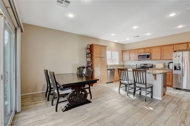 kitchen featuring light stone countertops, visible vents, a kitchen island, stainless steel appliances, and a kitchen breakfast bar