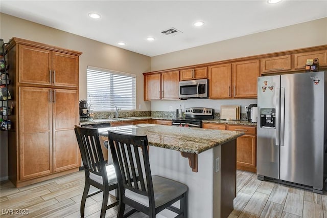 kitchen featuring stainless steel appliances, brown cabinets, a kitchen island, and visible vents