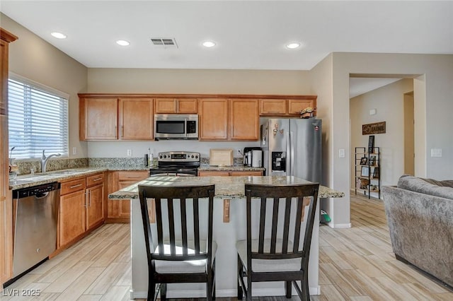 kitchen with visible vents, wood tiled floor, a kitchen island, a sink, and appliances with stainless steel finishes