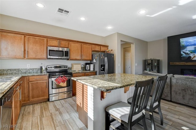 kitchen featuring brown cabinetry, visible vents, stainless steel appliances, and open floor plan