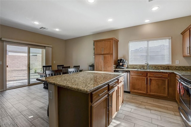 kitchen featuring visible vents, a sink, a kitchen island, stainless steel appliances, and dark stone counters