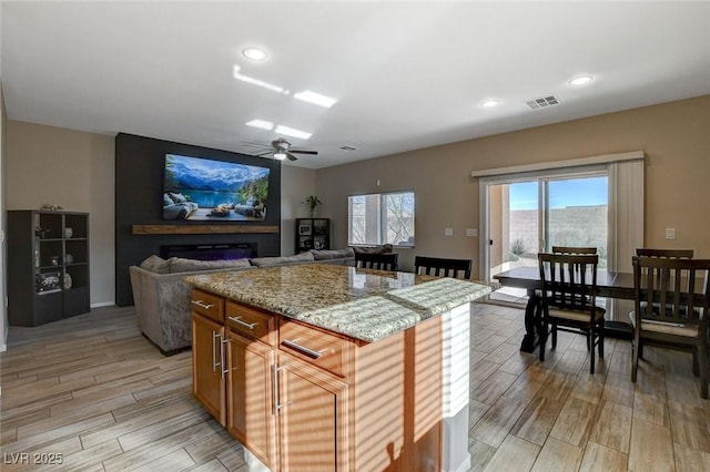 kitchen with light stone countertops, visible vents, a kitchen island, wood finish floors, and a fireplace