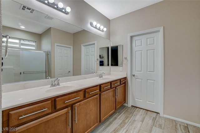 bathroom with wood finished floors, visible vents, double vanity, a stall shower, and a sink