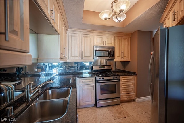 kitchen featuring a notable chandelier, a sink, stainless steel appliances, dark stone counters, and a raised ceiling