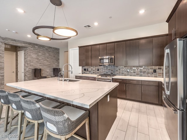 kitchen with visible vents, stainless steel appliances, dark brown cabinets, a kitchen breakfast bar, and tasteful backsplash