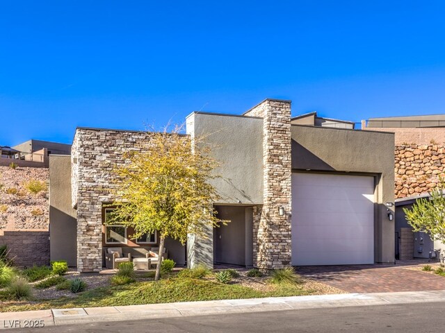 contemporary house with a garage, decorative driveway, stone siding, and stucco siding