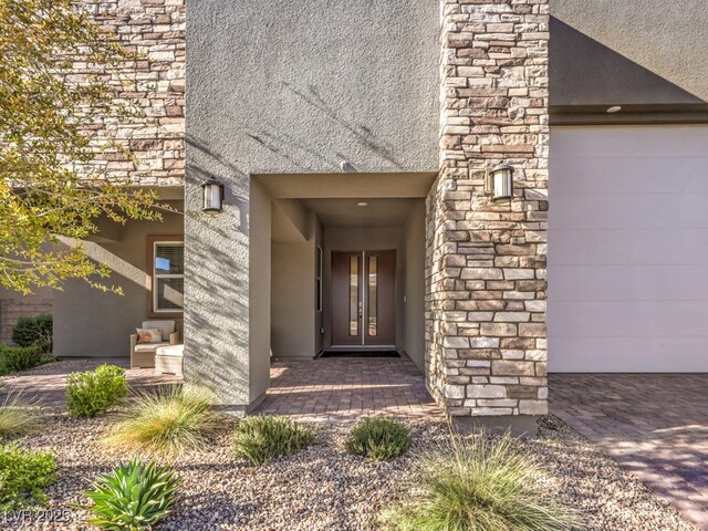 doorway to property featuring stone siding, stucco siding, and a garage