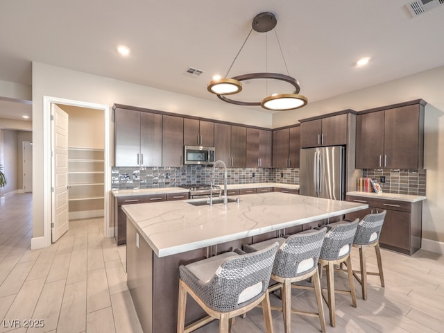 kitchen featuring visible vents, a center island with sink, stainless steel appliances, and a sink