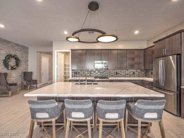 kitchen with light wood-type flooring, decorative backsplash, dark brown cabinetry, and appliances with stainless steel finishes