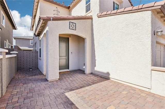 view of exterior entry featuring stucco siding and a patio