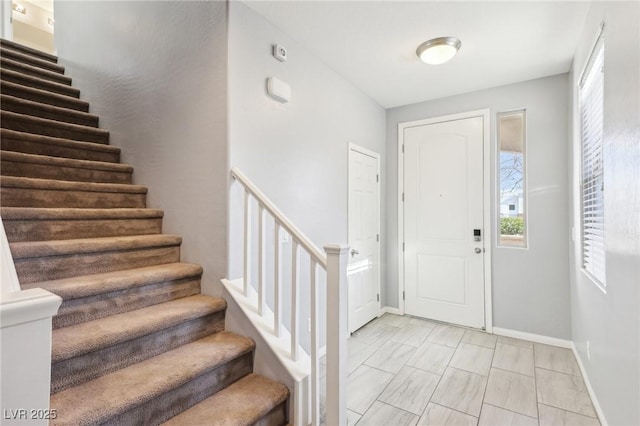 foyer entrance with stairs and baseboards