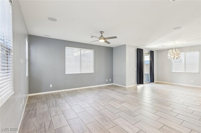 spare room featuring ceiling fan with notable chandelier and baseboards