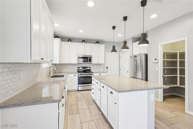 kitchen with a sink, a kitchen island, tasteful backsplash, appliances with stainless steel finishes, and white cabinets