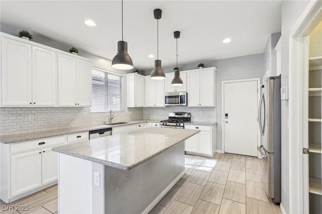 kitchen featuring a sink, a kitchen island, backsplash, white cabinetry, and appliances with stainless steel finishes