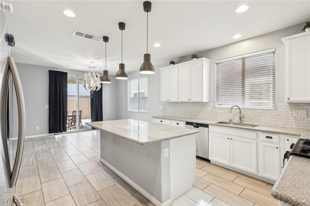 kitchen featuring visible vents, a kitchen island, a sink, appliances with stainless steel finishes, and tasteful backsplash