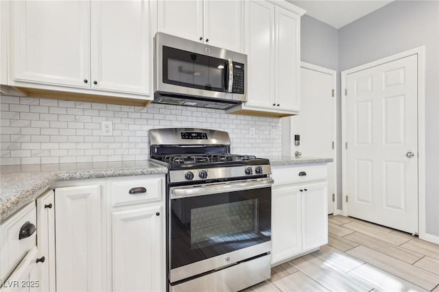 kitchen with light stone countertops, wood tiled floor, appliances with stainless steel finishes, white cabinetry, and backsplash