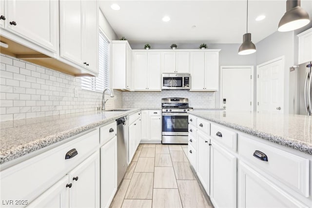 kitchen featuring a sink, hanging light fixtures, stainless steel appliances, white cabinetry, and tasteful backsplash