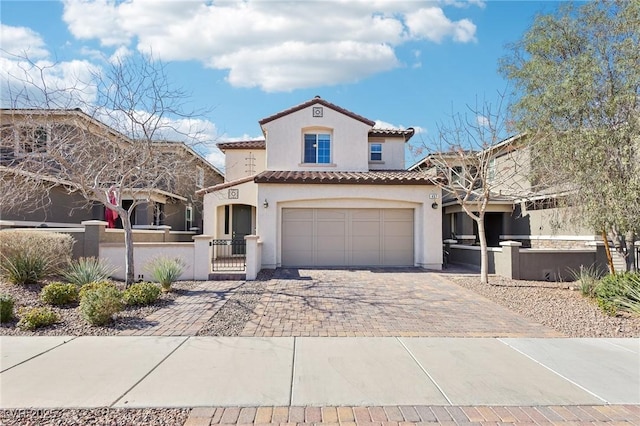 mediterranean / spanish-style home featuring stucco siding, a tile roof, a fenced front yard, decorative driveway, and an attached garage