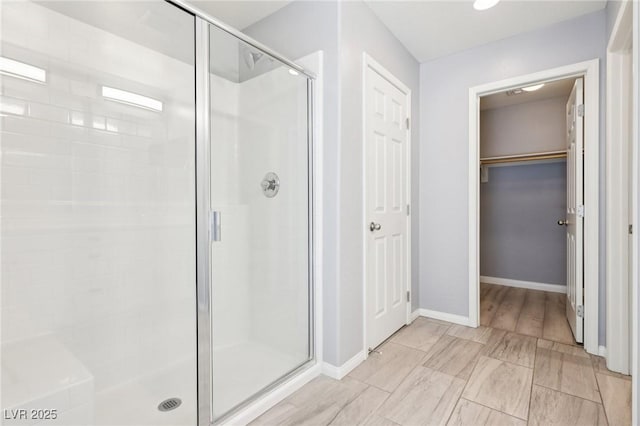 full bath with baseboards, a spacious closet, and a shower stall