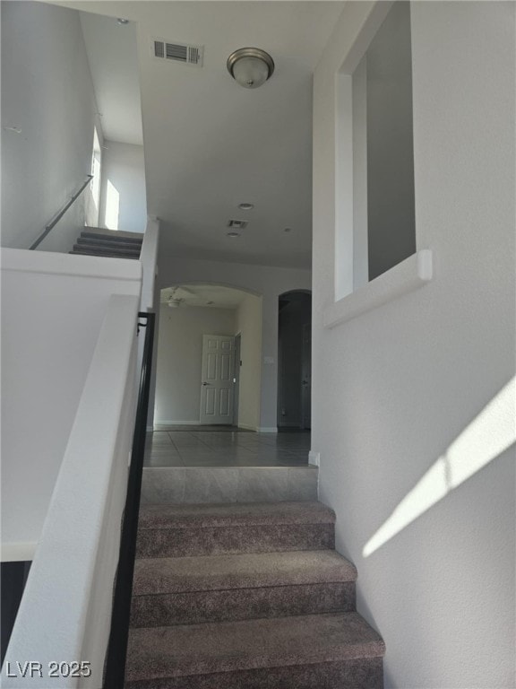 staircase featuring visible vents, arched walkways, and tile patterned flooring