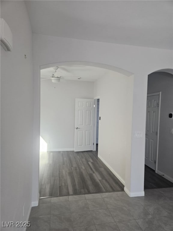 unfurnished room with baseboards, arched walkways, a ceiling fan, and a wall unit AC