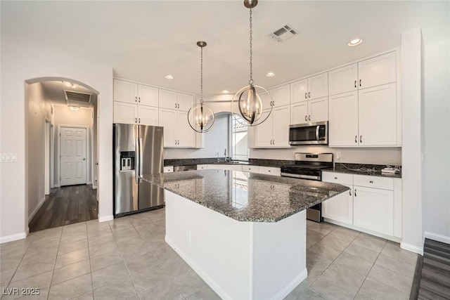 kitchen featuring visible vents, a kitchen island, white cabinetry, stainless steel appliances, and arched walkways