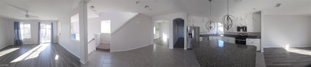 kitchen with dark countertops, stainless steel microwave, range with gas cooktop, arched walkways, and white cabinetry