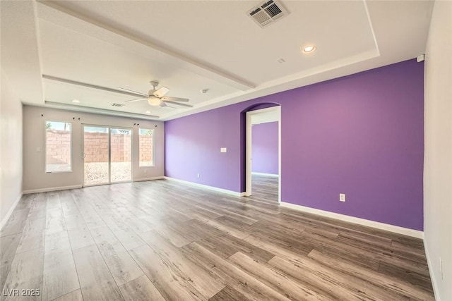 spare room with arched walkways, visible vents, a raised ceiling, and wood finished floors