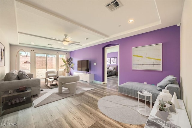 living area with wood finished floors, visible vents, baseboards, arched walkways, and a raised ceiling