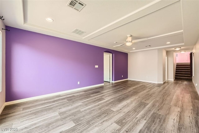 spare room with stairway, a ceiling fan, wood finished floors, visible vents, and arched walkways