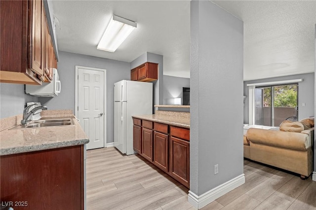 kitchen featuring a textured ceiling, white appliances, light wood-style flooring, and a sink