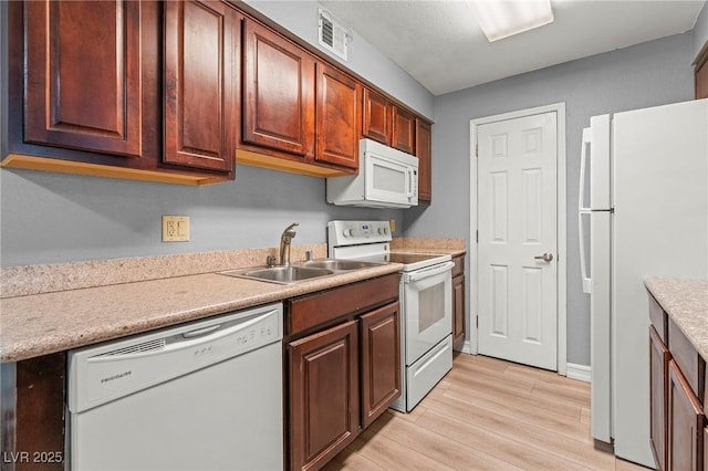 kitchen featuring a sink, white appliances, light wood-style floors, and light countertops