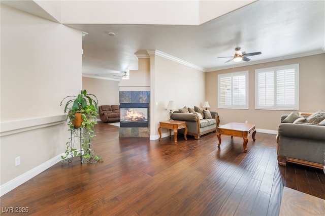 living room with wood finished floors, baseboards, a multi sided fireplace, ceiling fan, and ornamental molding