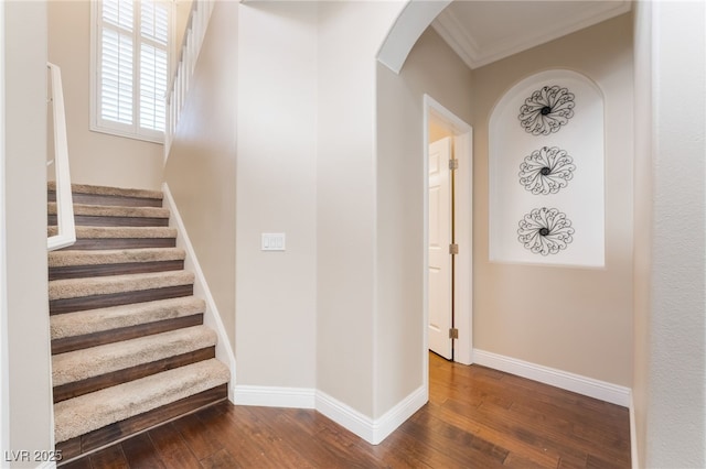 stairs with crown molding, arched walkways, baseboards, and wood-type flooring