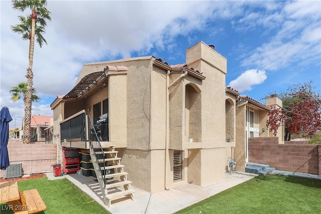 view of side of property featuring stucco siding, central air condition unit, a lawn, fence, and a chimney