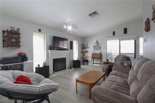 living area featuring vaulted ceiling, plenty of natural light, light wood-style floors, and visible vents