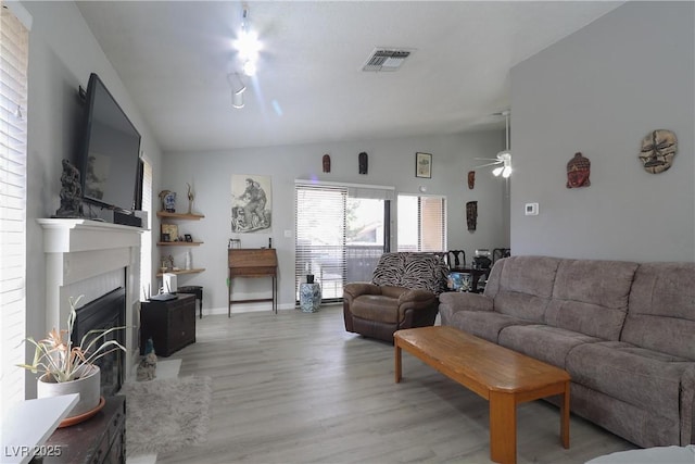 living room with light wood-type flooring, visible vents, lofted ceiling, and a glass covered fireplace